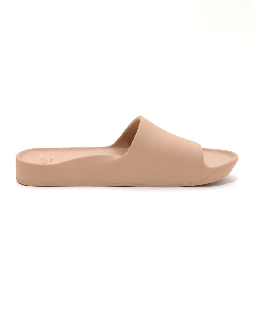 A side profile of the Archies Archie Slide in Tan shows a single open-toe sandal with a wide band, crafted from comfortable closed cell foam, set against a white background.