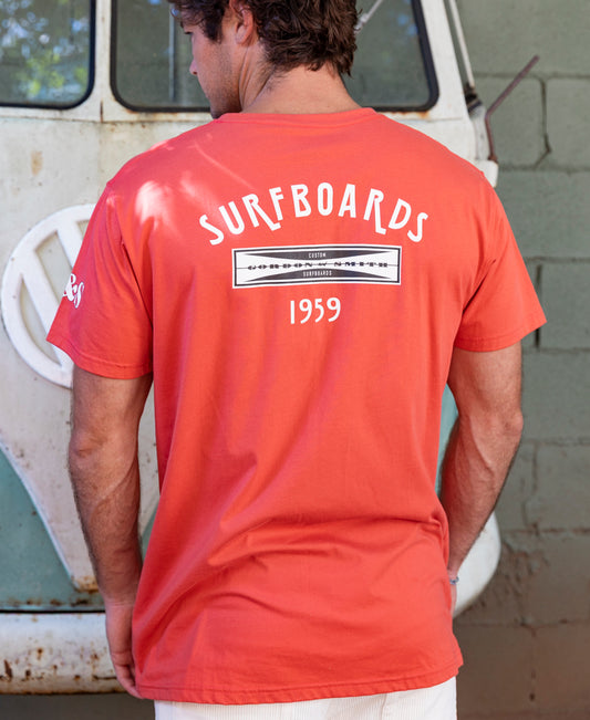 A man wearing a Gordon & Smith G&S Surfboards Tee in Wash Red stands with his back to the camera in front of a vintage Volkswagen van.