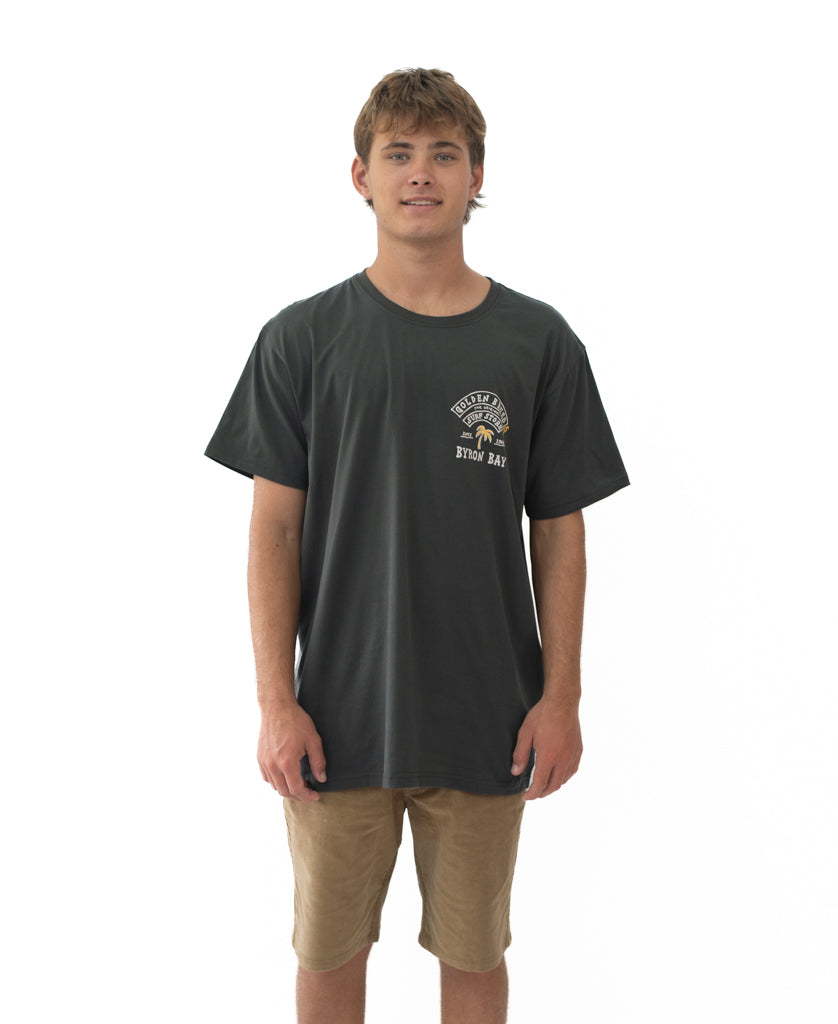 Young man wearing a Byron Herring Tee | Wash Black with a small surf-inspired logo on the chest, paired with casual tan shorts, styled in a simple surfwear look.