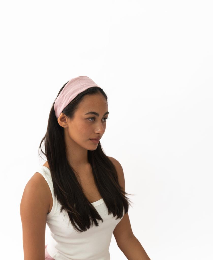 A woman with long dark hair wears the Lazy Beach Head Scarf in Blush Linen and a white tank top, seated against a plain white background.