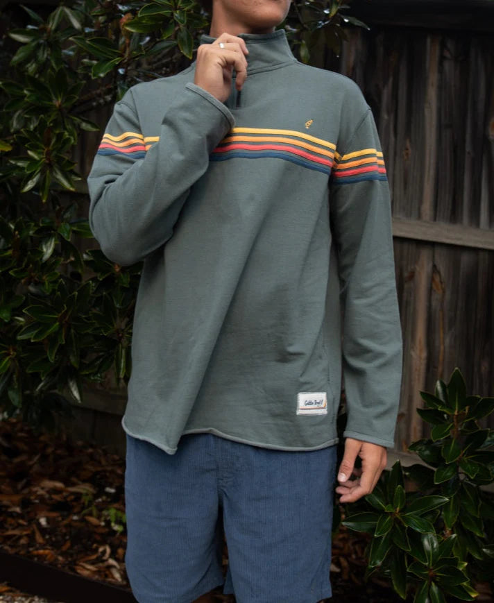 Person outdoors wearing a retro-style pullover with colorful stripes on the chest and Floyd Cord Elastic Waist Walkshort | Vintage Navy, standing near green foliage and a wooden fence.