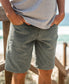 A person wearing a grey t-shirt and Golden Breed Floyd Cord Walkshort in Khaki stands outdoors near a beach with hands in pockets.