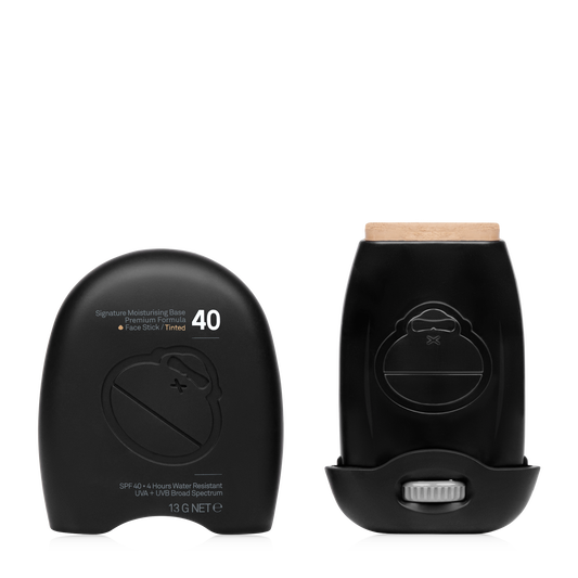 Two black Sun Bum Signature SPF40 Tinted Stick (13g) containers—one open to show the product—feature minimalist packaging. This mineral sunscreen provides broad spectrum facial protection.