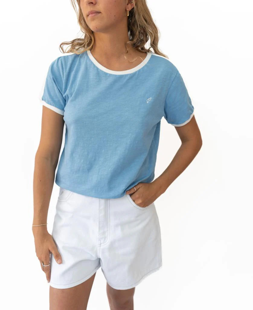 Woman wearing a Retro Ringer Tee | Azure with white trim on the sleeves and neckline, paired with white shorts, styled for a casual, surf-inspired look.
