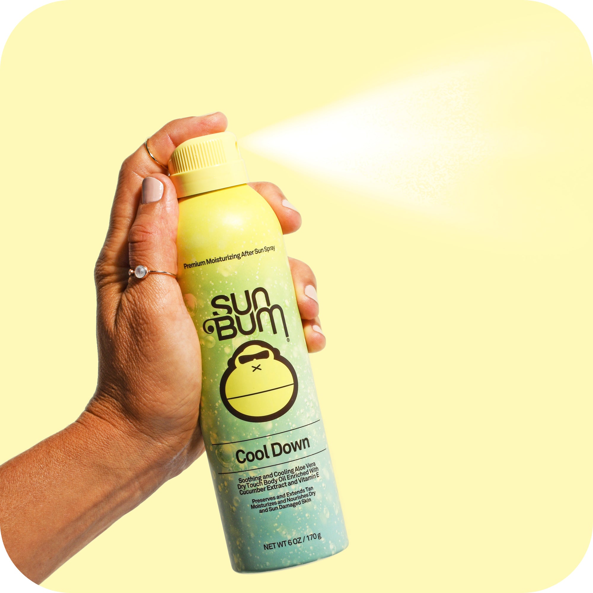 A hand sprays Sun Bum Aloe Spray | 177ml, a non-greasy formula with Vitamin E, against a yellow background.