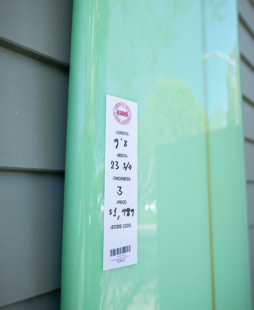 A user-friendly lime G&S 98 Easy Rider Polish Finish longboard by Gordon & Smith, priced at $1,799 with dimensions and barcode on the tag, leaning against a wall.