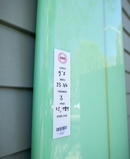 A user-friendly lime G&S 98 Easy Rider Polish Finish longboard by Gordon & Smith, priced at $1,799 with dimensions and barcode on the tag, leaning against a wall.