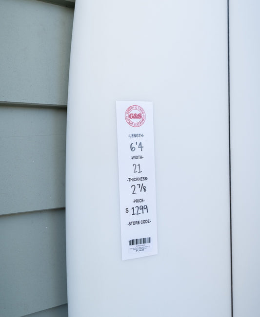 A white Gordon & Smith G&S 64 Power Twin Matte Finish board (64 length, 21 width, 2 7/8 thickness) priced at $1,299 leans against the wallโperfect for quality seekers or surf freight specialists.