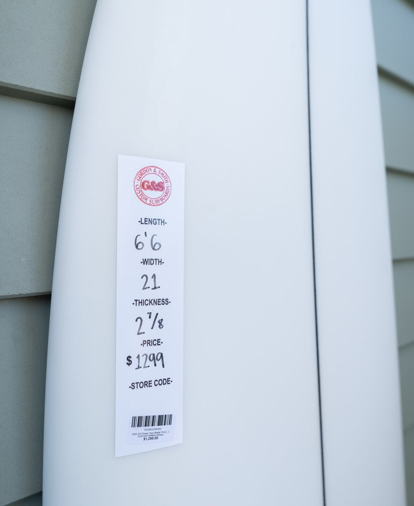 The Gordon & Smith G&S 66 Power Twin Matte Finish | White surfboard, labeled 6’6” x 21” x 2 1/8”, with a medium rocker for performance, priced at $1299, leans against a wall.