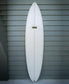A G&S 76 Cool Tool Mid Twin surfboard by Gordon & Smith in off white, celebrated for its wave-catching prowess, stands upright against a gray horizontal siding wall.