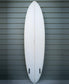 The G&S 76 Cool Tool Mid Twin by Gordon & Smith, in off white with two black fin boxes, stands upright against a green horizontal panel wall, renowned for its excellent wave catching performance.