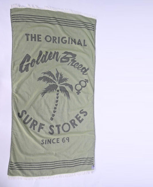 The GB Otto Towel | Green by Golden Breed is a soft Turkish cotton towel with fringe edges, featuring The Original Golden Breed Surf Stores Since 69 and a palm tree graphic in the center.