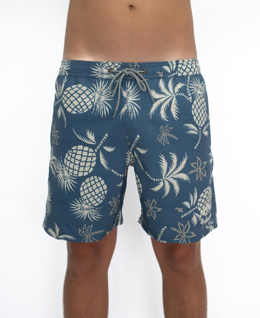 A person wears Golden Breeds Pine-Palm Elastic Waist Boardie in Dusty Blue, made from recycled polyester with a white pineapple and palm tree print, shown waist to above the knees against a plain white background.