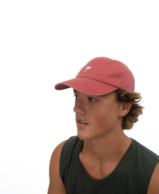 A young person wearing a sleeveless dark shirt and the Golden Breed Palm Cap | Wash Red with a palm tree logo looks to the side against a plain white background.