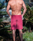 A shirtless man stands outdoors with his back to the camera, wearing Golden Breed’s Floyd Cord Walkshort in Scarlet. Palm plants and a building are visible in the background.