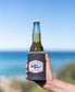 A hand holds a beer in a Golden Breed Ray Stubby Holder | Wash Black by Golden Breed, with the ocean and blue sky in the background.