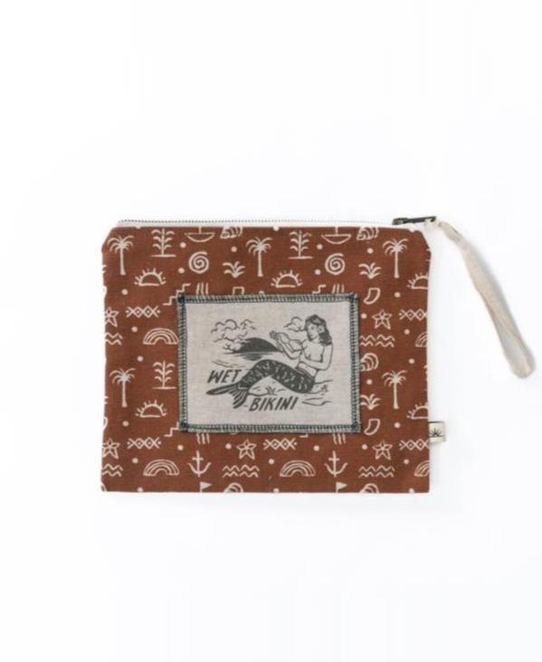 The Bomba WET BIKINI Sumba Alchemy bag is brown with white beach-themed symbols and a central patch featuring a woman. It has a zip closure and waterproof interior to keep your beach essentials dry.