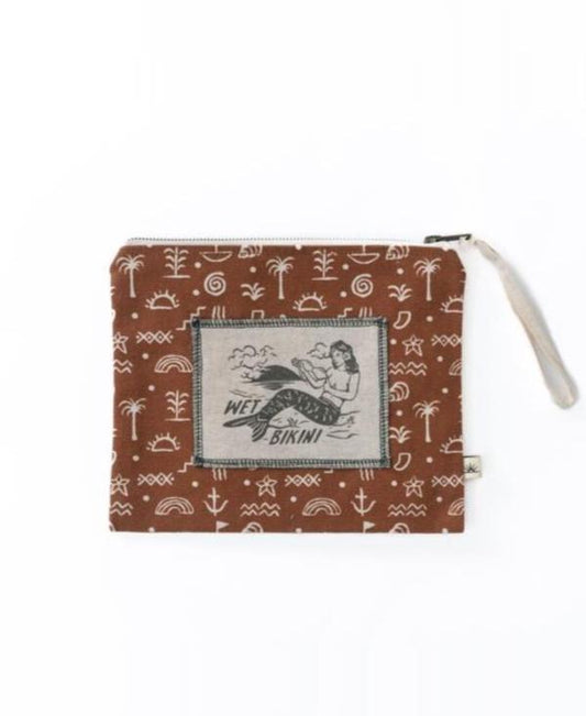 The Bomba WET BIKINI Sumba Alchemy bag is brown with white beach-themed symbols and a central patch featuring a woman. It has a zip closure and waterproof interior to keep your beach essentials dry.