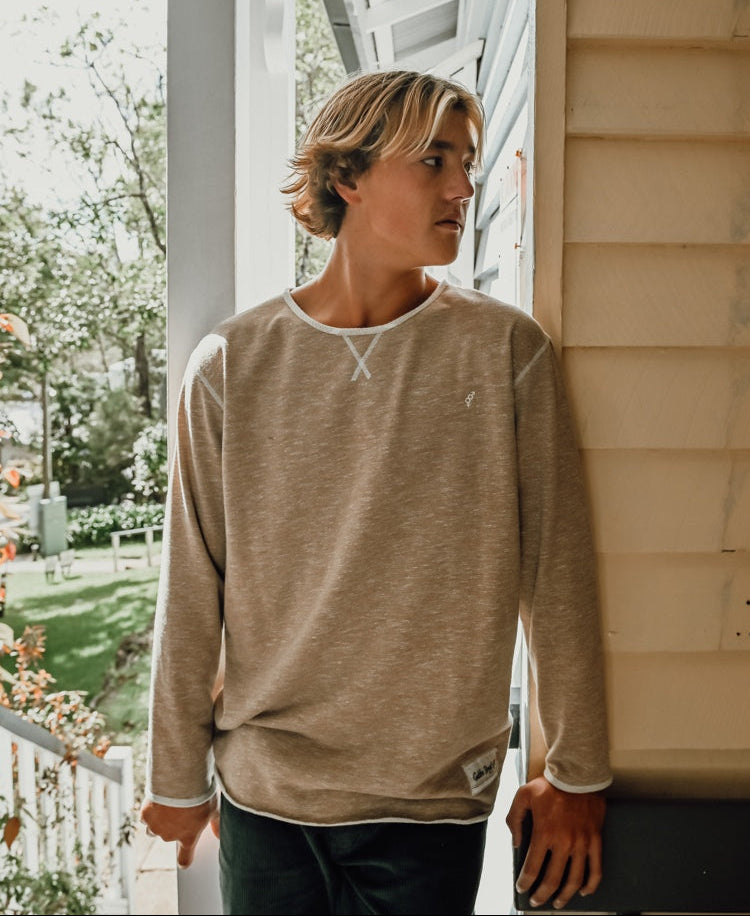 A young person with shoulder-length hair wears the Golden Breed Classic Rag Top in Coffee Marle, standing on a porch and looking to the side.