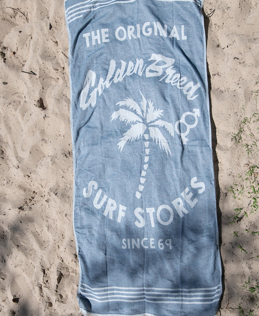 The GB Otto Towel | Navy by Golden Breed, made from soft Turkish cotton, features a palm tree illustration and the text The Original Golden Breed Surf Stores Since 69. Fast-drying—perfect for beach days.