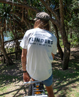 Wearing a Golden Breed Flinders Old School Tee | Off White, a person sits on a bike in a park, blending classic 100% cotton comfort with laid-back outdoor vibes.