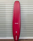 The Gordon & Smith G&S Log Cardinal 98 longboard in red stands upright against a light gray, horizontally paneled wall.