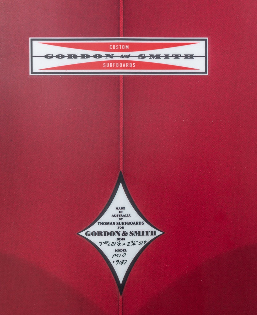 A close-up of a red G&S Mid length Cardinal 76 surfboard by Gordon & Smith, showing logos and handwritten specs such as model, dimensions, and serial number.
