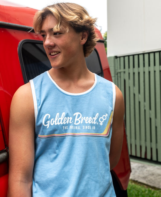 A young man in a Golden Breed Retro Ringer Muscle Top in Azure Blue with classic retro print stands before a red vehicle, glancing left, with a fence and building in the background.