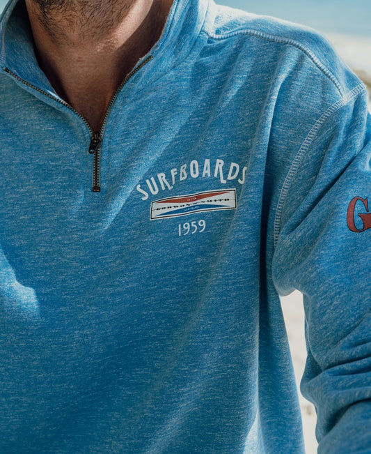 A person wearing the Gordon & Smith G&S 1/4 Zip Surfboards Rag Top in Sky Marle, featuring a SURFBOARDS 1959 graphic on the chest.