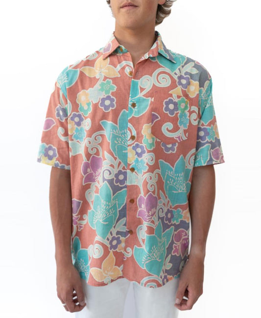 A person wears the Golden Breed Batik Shirt | Roseโa short-sleeve, button-up batik shirt with a colorful floral and swirl patternโpaired with white pants.