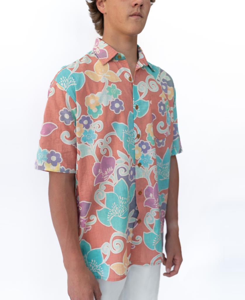 A person wearing a short-sleeved Golden Breed Batik Shirt | Rose, featuring a colorful floral print, stands against a plain white background.