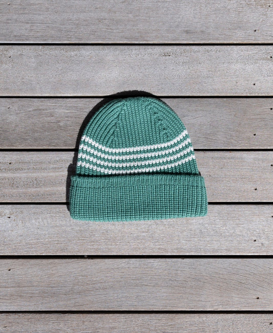 The Golden Breed Beach Boy Wool Beanie | Clover, an Australian Made green Merino Wool beanie with white stripes, is laid flat on a wooden surface.