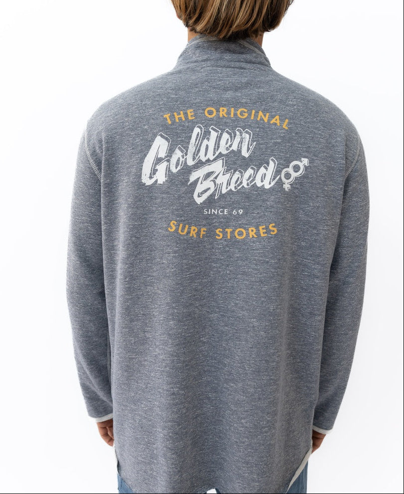 A person wears a navy marle Golden Breed Break 1/4 Zip Rag Top featuring “The Original Golden Breed Surf Stores Since 69” in white and yellow on the back, crafted from soft French Terry for extra comfort.