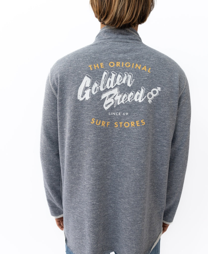 A person wears a navy marle Golden Breed Break 1/4 Zip Rag Top featuring “The Original Golden Breed Surf Stores Since 69” in white and yellow on the back, crafted from soft French Terry for extra comfort.