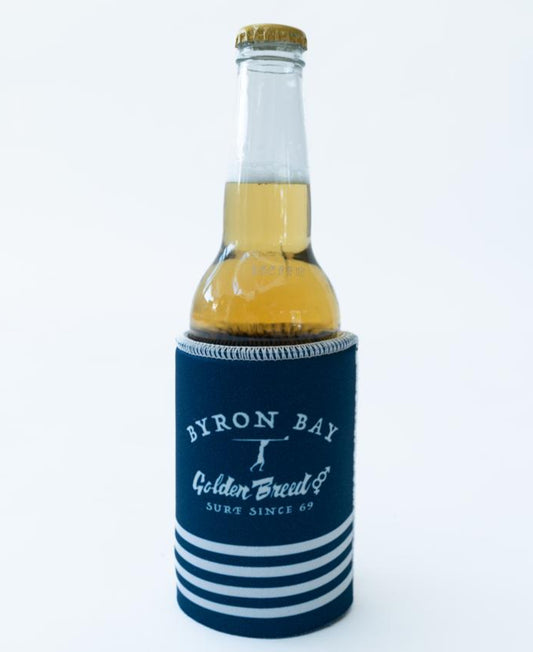 A clear glass beer bottle with a gold cap sits in a Golden Breed Byron Stubby Beach Boy | Navy holder against a plain white background.