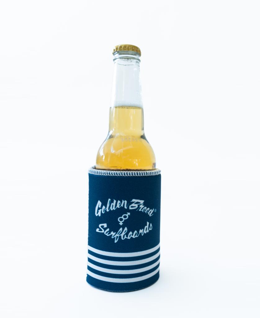 A light beverage in a clear glass bottle rests inside the Byron Stubby Beach Boy | Navy holder by Golden Breed, featuring white bottom stripes—perfect for relaxing in Byron Bay.