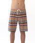 A person wears Golden Breeds Daze Boardie | Stripe, multicolored striped boardshorts with a white drawstring made from recycled polyester, standing against a plain white background with torso partially out of frame.