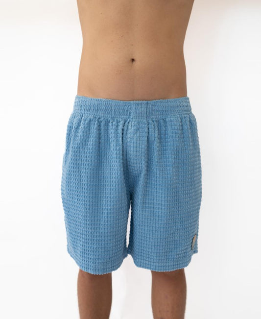 A person stands arms raised, shown from mid-chest to knees, wearing Golden Breed’s El Solito Walkshort in Azure Blue with an elastic waist, against a plain white background.