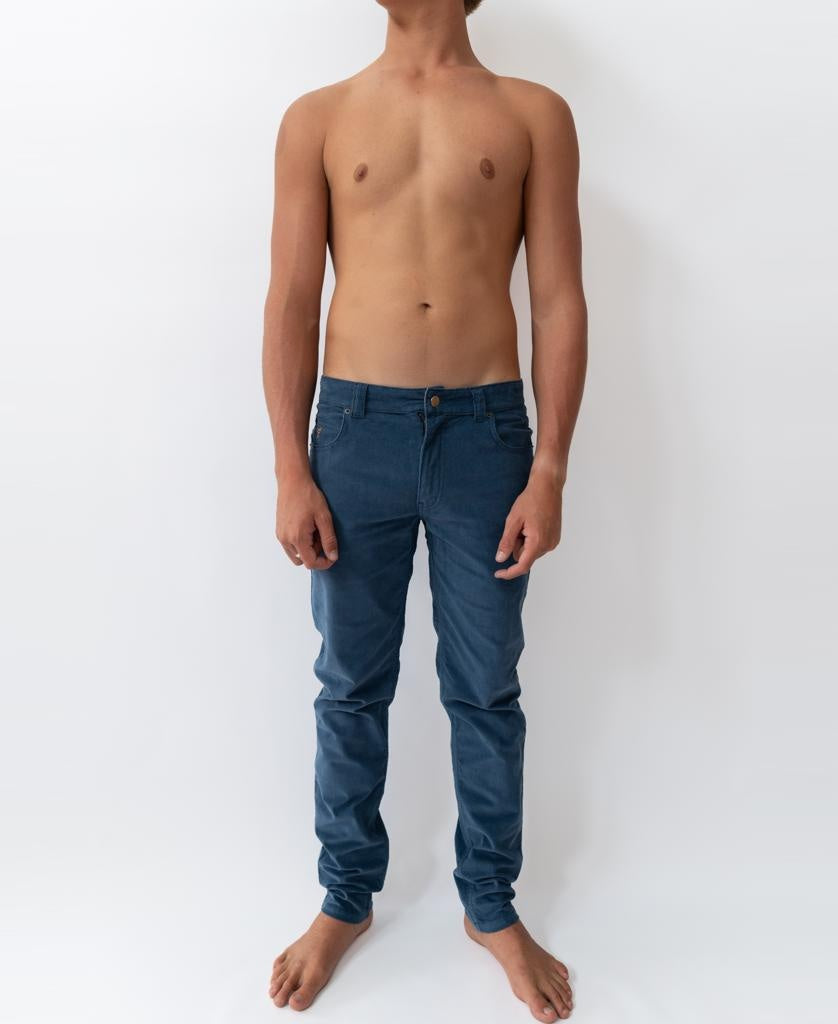 A shirtless person stands barefoot against a plain white background, wearing Golden Breeds Felix Stretch Cord Pant in Dusty Blue.