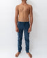 A shirtless person stands barefoot against a plain white background, wearing Golden Breeds Felix Stretch Cord Pant in Dusty Blue.