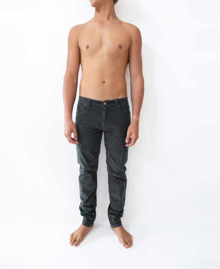 A shirtless person stands barefoot against a white background, wearing Golden Breed Felix Stretch Cord Pant in Wash Black. Their arms are relaxed at their sides and their head is turned slightly to the left.