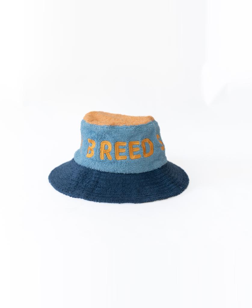 The Ferry Terry Bucket Hat | Azure Blue by Golden Breed features tan terry towelling, bold orange BREED lettering on the front, and is displayed on a white background—a timeless classic.