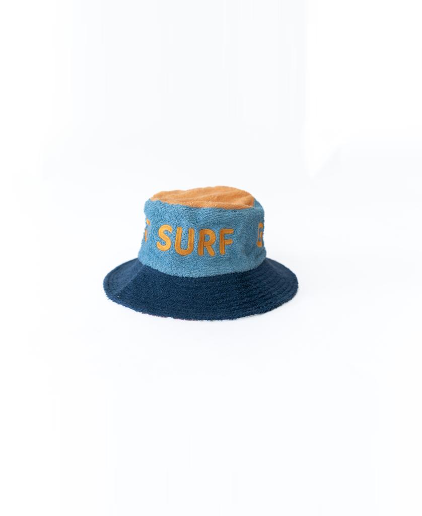 The Ferry Terry Bucket Hat by Golden Breed features azure blue and tan color blocks with yellow SURF lettering on the front, shown on a white background.