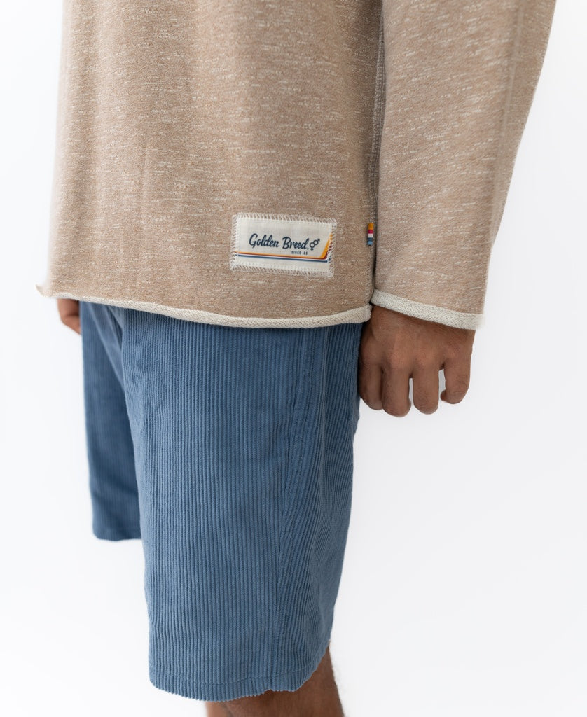 A person wears a mocha marle Golden Breed Fin 1/4 Zip Rag Top with light blue corduroy shorts, shown from shoulder to knee against a white background.