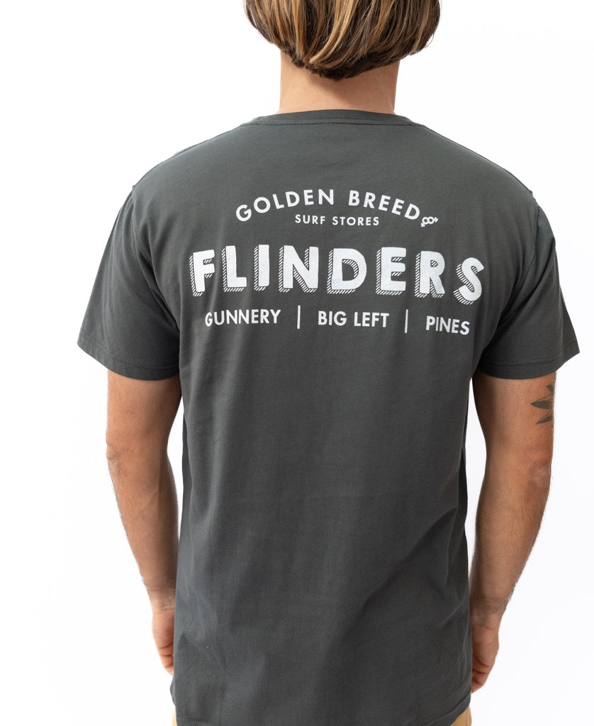 Someone wearing a Golden Breed Flinders Old School Tee | Wash Black, part of the 100% Cotton Location Tees collection, featuring GOLDEN BREED SURF STORES FLINDERS GUNNERY | BIG LEFT | PINES printed on the back.