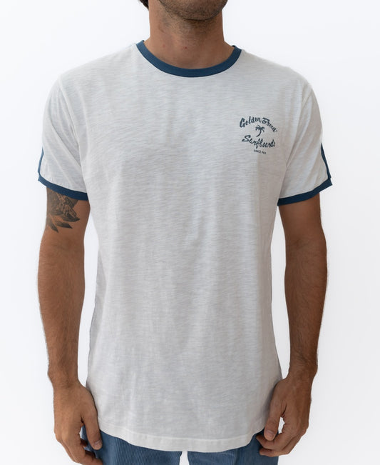A person wears an off white Golden Breed Flinders Landy Tee ringer t-shirt with blue trim and Golden Boys Surfboards text on the left chest, crafted from soft cotton slub, standing against a plain background.