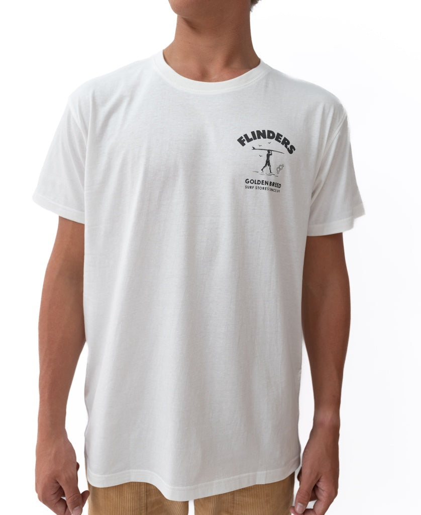 Someone wearing the Golden Breed Flinders Shanty Tee in Off White, featuring a small Flinders Golden Fried logo and text on the left chest, stands against a white background—classic surf store style.