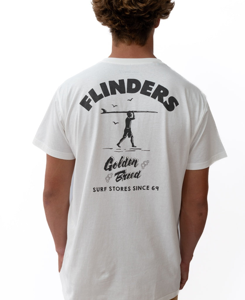 Someone wearing the Golden Breed Flinders Shanty Tee in off white, featuring a black FLINDERS surfer graphic and SURF STORES SINCE 69 printed on the back.
