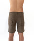 A person faces away from the camera wearing Golden Breed’s Floyd Cord Walkshort in Wash Brown, featuring a structured waist and no shirt, set against a white backdrop.