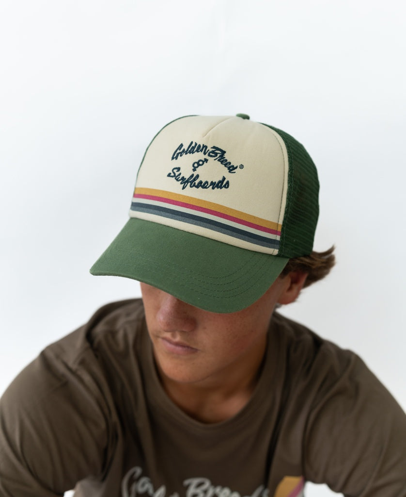 A person wearing a Khaki GoJo Trucker Cap by Golden Breed with multicolored stripes, adjustable strap, and “Golden State & Sunfriends” text, paired with a brown t-shirt.